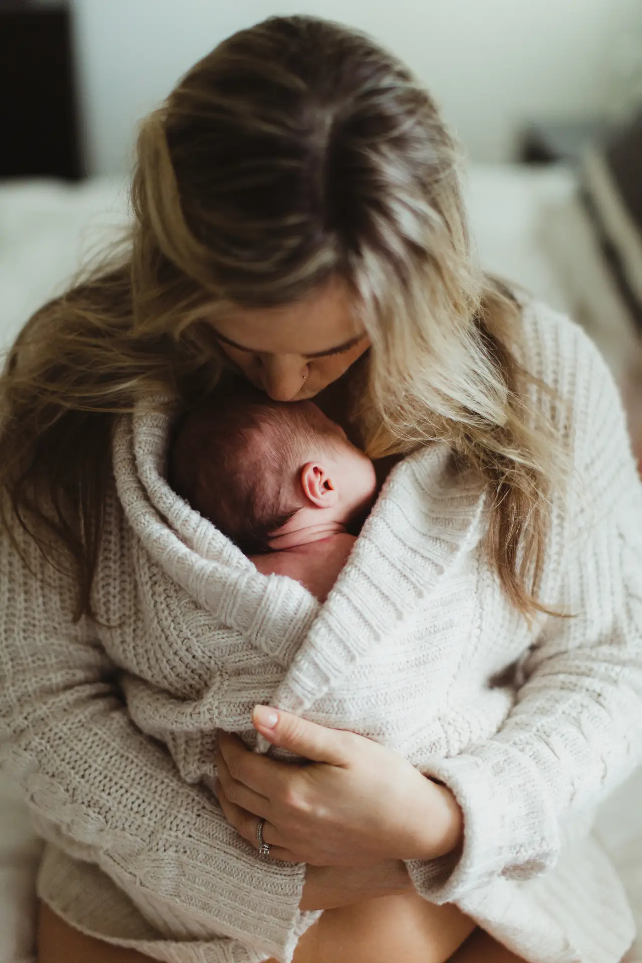 mid adult woman kissing new born baby daughter wrapped in cardigan