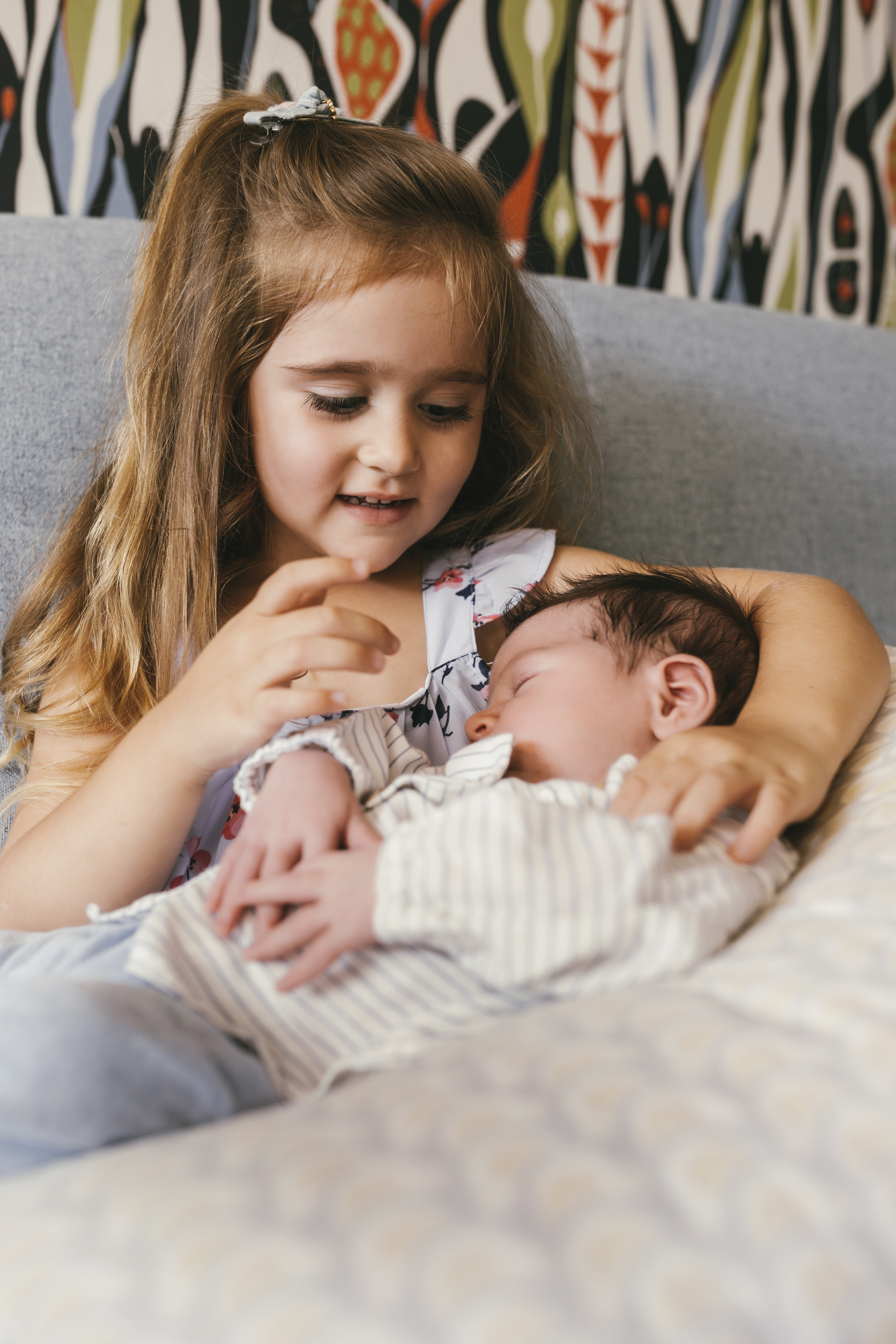 girl sitting on couch looking at newborn baby brother